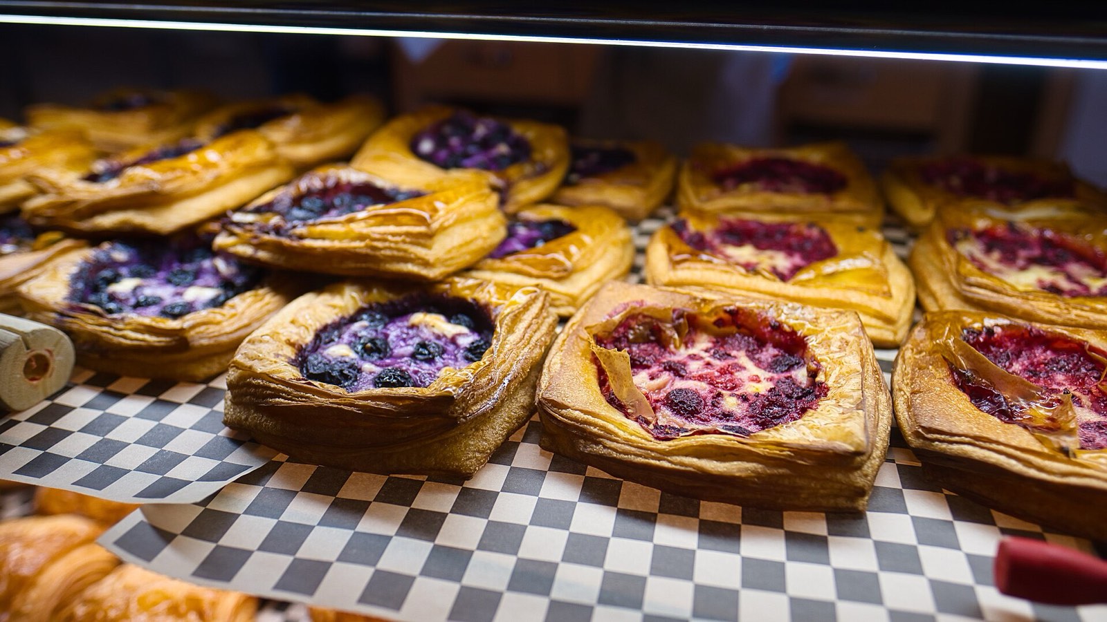 Blueberry and raspberry danishes lined up in a bakery case on checkered paper