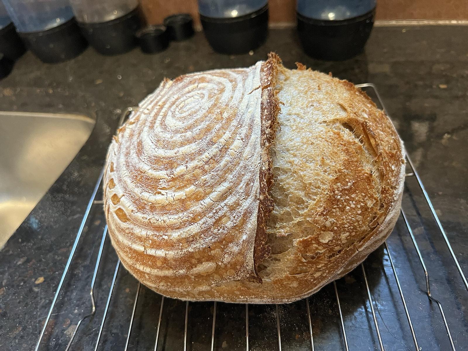 A round sourdough loaf with a flour-dusted spiral score, cooling on a wire rack