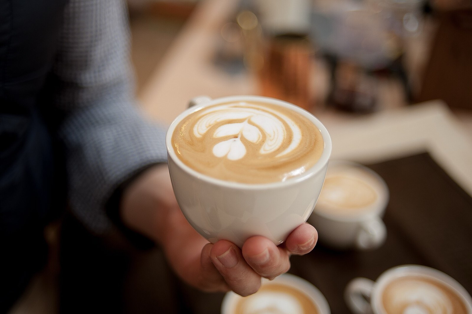 A hand holding a white cup of latte with a tulip of foam