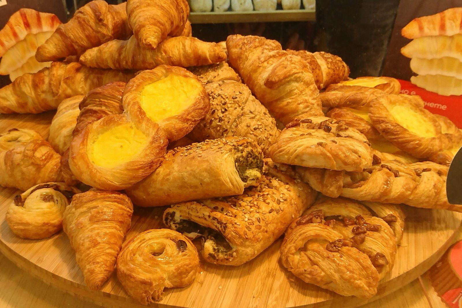 A wooden board piled with croissants, custard danishes and chocolate pastries